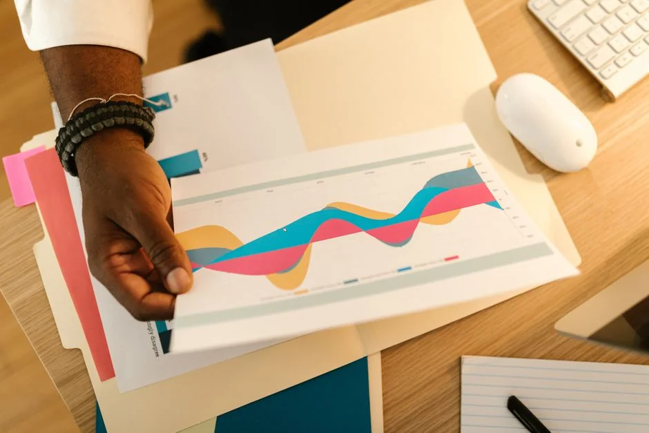 A person reviews stock market data using a smartphone and laptop while indoors.